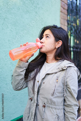 young slim latina woman, drinking water with her eyes up, copy space
