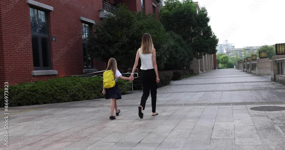 Happy little caucasian blonde girl seven years old in uniform with yellow backpack going back to school after summer vacations or Coronavirus covid-19 quarantine with young mother. 4k slow motion Happy little caucasian blonde girl seven years old in uniform with yellow backpack going back to school after summer vacations or Coronavirus covid-19 quarantine with young mother. 4k slow motion