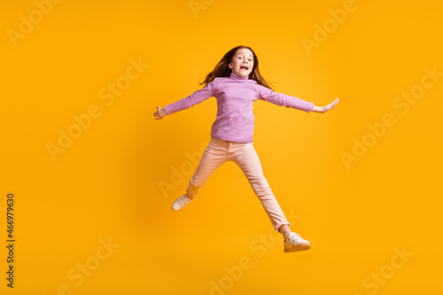 Full size photo of happy good mood excited energetic little girl jumping having fun isolated on yellow color background