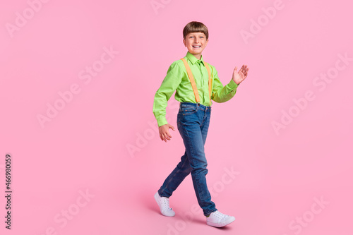 Full length body size view of attractive cheerful boy walking waving isolated over pink pastel color background