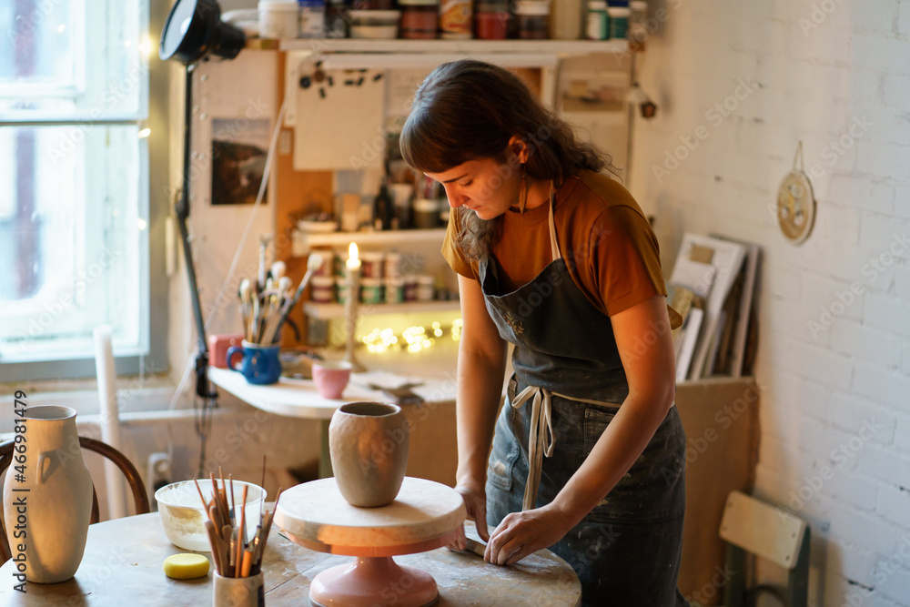 Art therapy for hobby or small business: young woman work in ceramics studio on handicraft jar production for handmade pottery shop. Artisan female shaping tableware from raw clay in workshop space - obrazy, fototapety, plakaty 