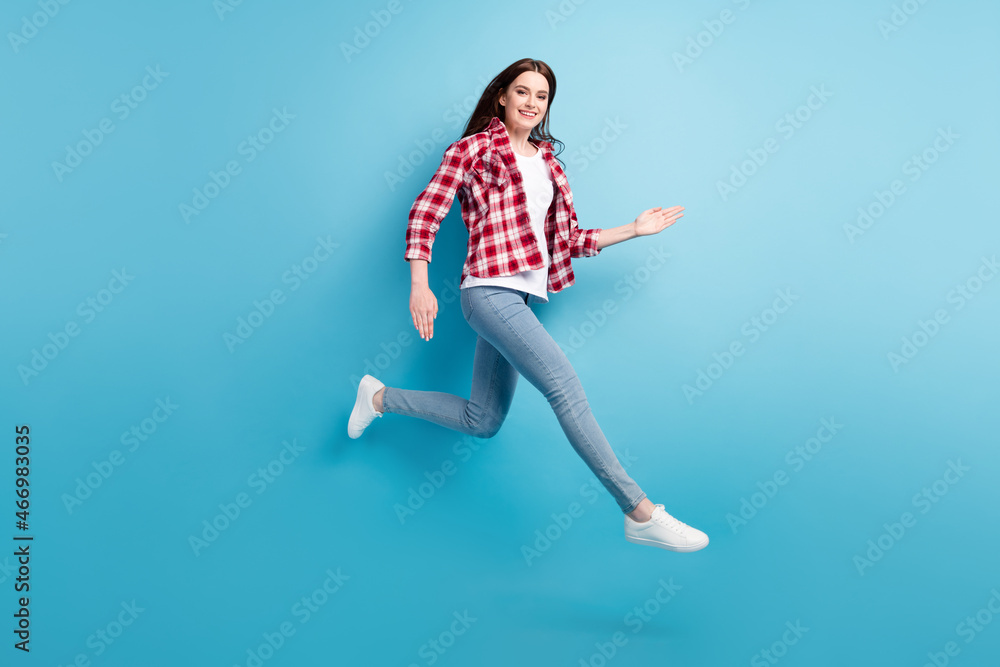 Full body photo of happy cheerful young woman jump up run empty space sale isolated on blue color background Full body photo of happy cheerful young woman jump up run empty space sale isolated on blue color background