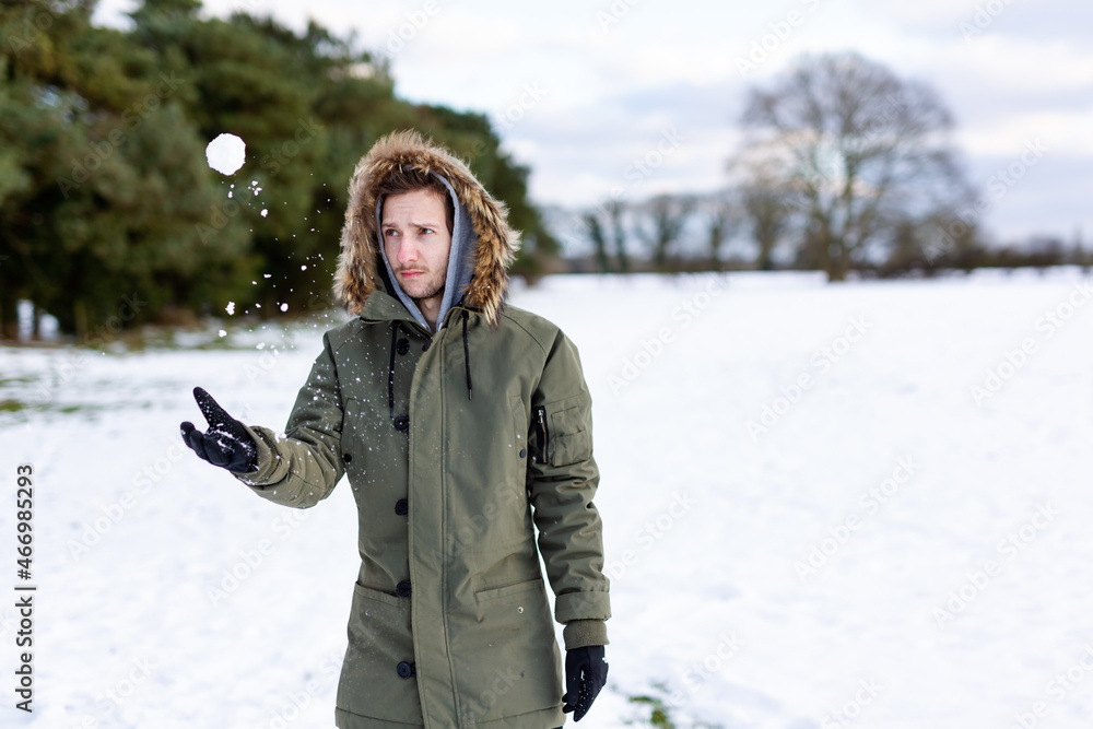 A determined looking young man with a snowball in hand ready to throw it during a snowball fight. He is in a snow covered wintery landscape A determined looking young man with a snowball in hand ready to throw it during a snowball fight. He is in a snow covered wintery landscape