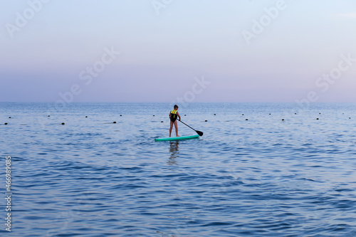 Boy ride a paddle board on the sea at sunset. Supboard water sport activity