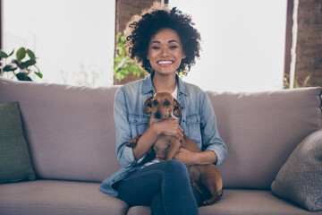 Photo of young cheerful african couple happy positive smile hug animal pet best friend dog sit couch indoors