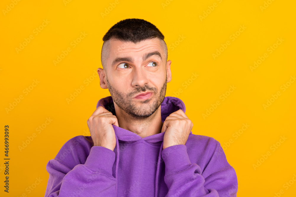 Photo of young doubtful curious man look empty space hold hands hood casual isolated on yellow color background Photo of young doubtful curious man look empty space hold hands hood casual isolated on yellow color background