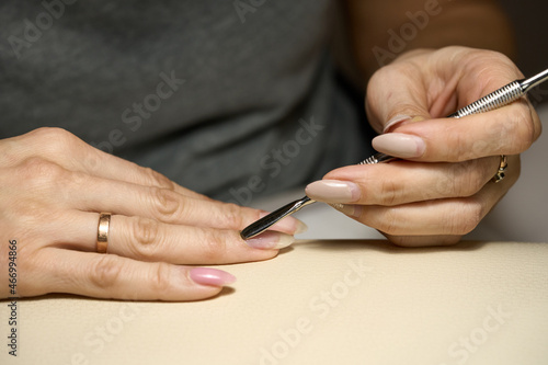 Woman doing manicure for herself with cuticle stainless stick. Closeup high quality photo.