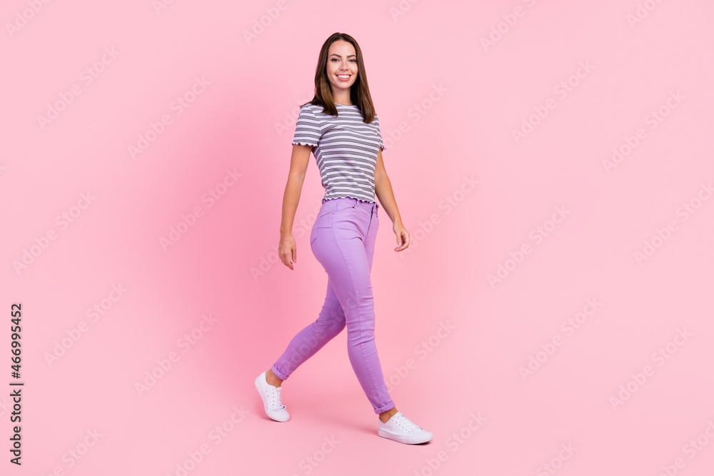 Photo of adorable shiny young lady wear striped outfit smiling walking isolated pink color background Photo of adorable shiny young lady wear striped outfit smiling walking isolated pink color background