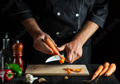 Cook peels carrots for vegetable soup in a restaurant kitchen. Close-up hands of the chef during work. Carrot diet
