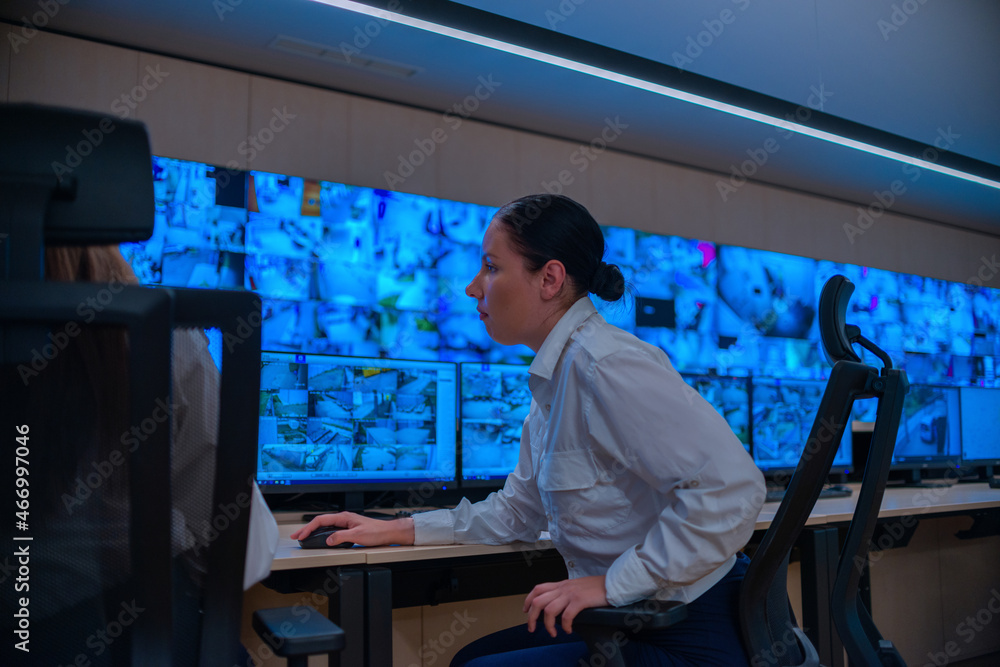 Group of Security data center operators (administrators) working in a group at a CCTV monitoring room while looking at multiple monitors ( computer screens)