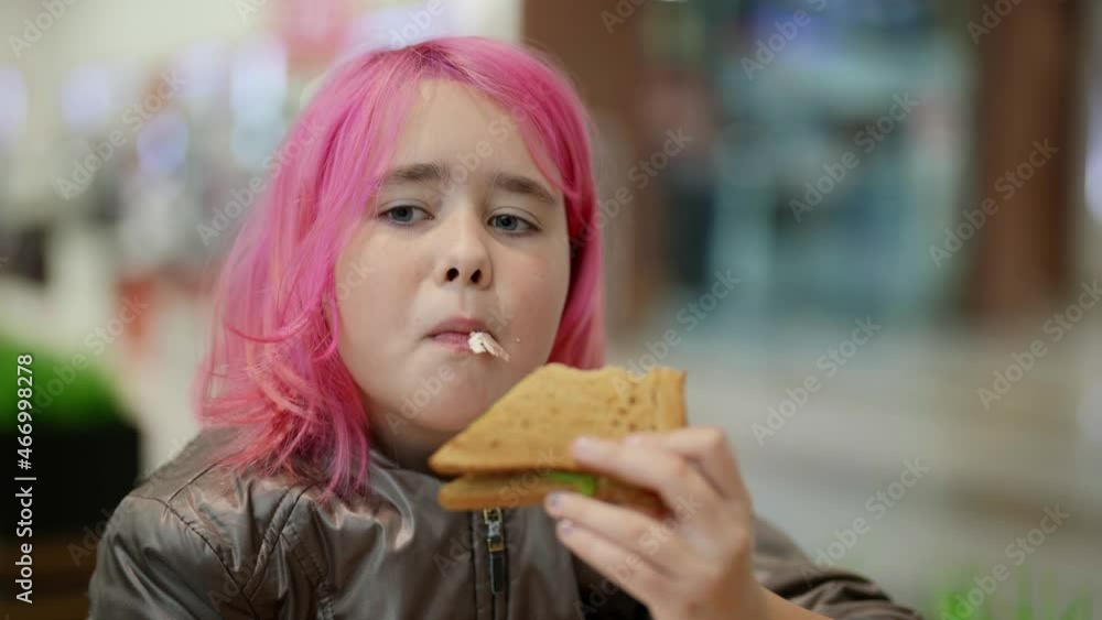 Sad homeless teenager with pink hair eats a sandwich in a cafe Sad homeless teenager with pink hair eats a sandwich in a cafe
