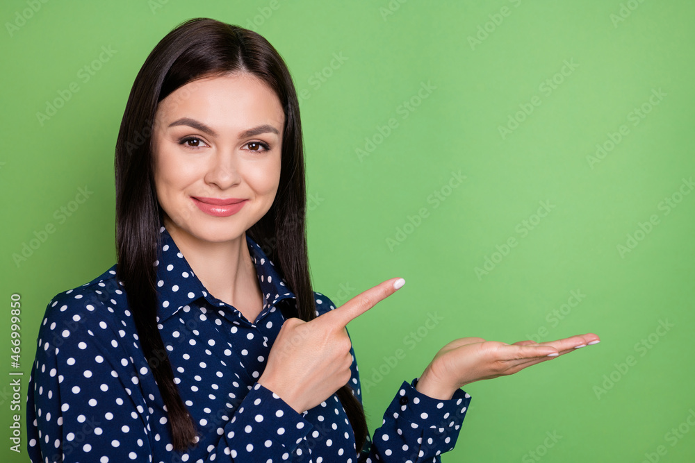Photo of girl indicate finger hand hold empty space object wear dotted blouse isolated on green color background Photo of girl indicate finger hand hold empty space object wear dotted blouse isolated on green color background