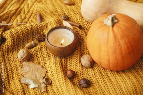 Hello fall season. Stylish yellow knitted sweater with burning candle  pumpkins  autumn leaves and nuts. Cozy autumn slow living. Happy Thanksgiving and Halloween.
