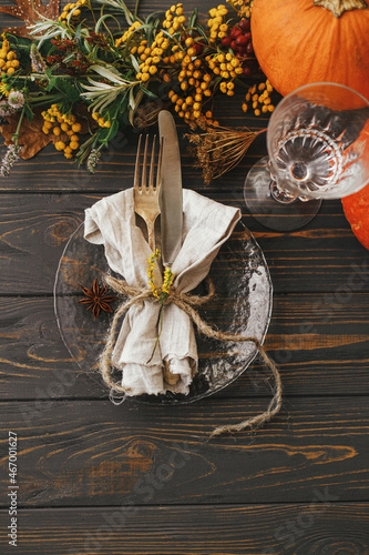Thanksgiving dinner rustic table setting. Modern plate with vintage cutlery, linen napkin, herb and glass on wooden table with pumpkins and autumn flowers arrangement. Eco friendly catering