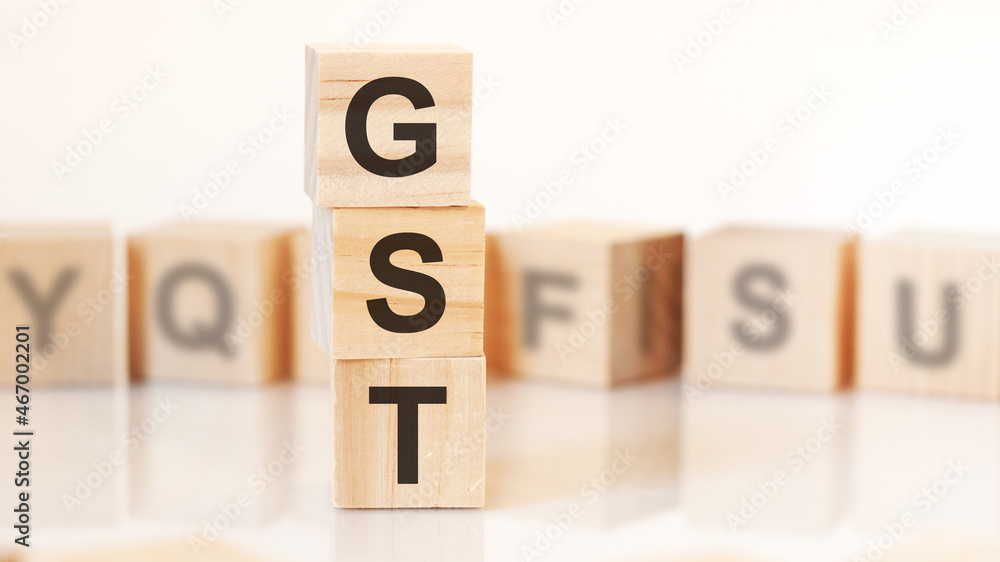wooden cubes with letters GST arranged in a vertical pyramid, on the light background, reflection surface, concept wooden cubes with letters GST arranged in a vertical pyramid, on the light background, reflection surface, concept