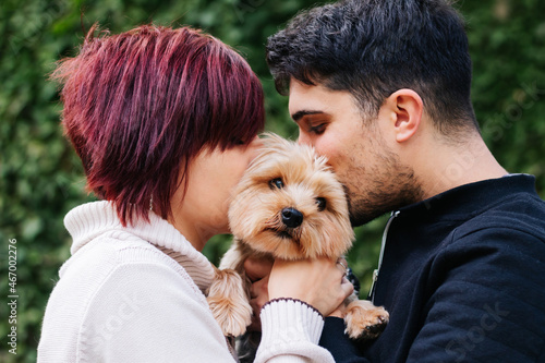 Young 20s loving couple, giving a kiss to their pet Yorkshire terrier dog on Valentine's Day. concept of family, pet care, adoption of animals and love.