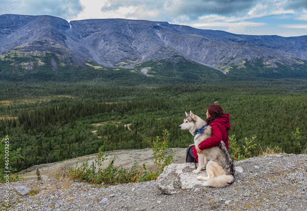 Young female sitting with siberian husky dog in mountains