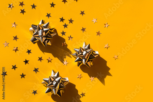 Gift silver bow with stars composition on monochrome yellow background. Winter, sale and seasonal concept. Merry Christmas, New Year banner. flat lay, top view. Space or place for text © makanna