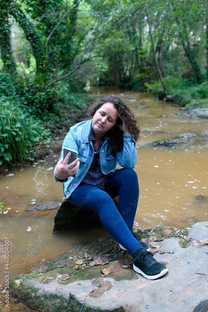 Vertical photo of woman resting sitting by a stream while using her smartphone. Vertical photo of woman resting sitting by a stream while using her smartphone.