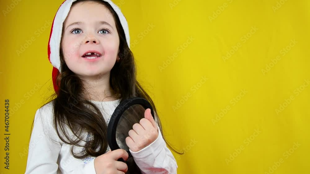 Happy child in a santa hat. Child in a New Year's hat on a yellow background. Little girl with a gift on a yellow background. New year concept. Online shopping. Children's gift shop