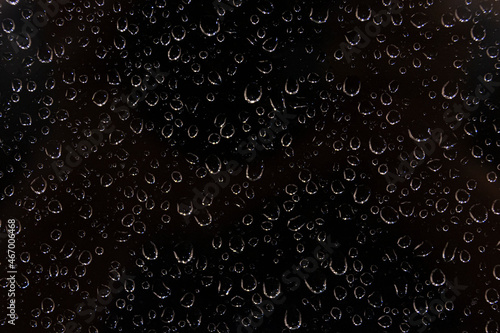 Closeup Of Water Drops Falling On Window In Rainy Weather At Night. Abstract View On Black Background Through Glass Covered With Condensation.