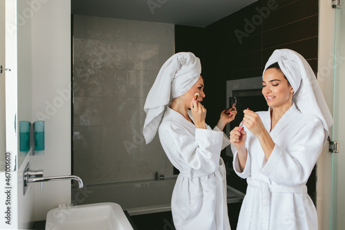 Two female friends wearing bathrobe and applying makeup in the bathroom