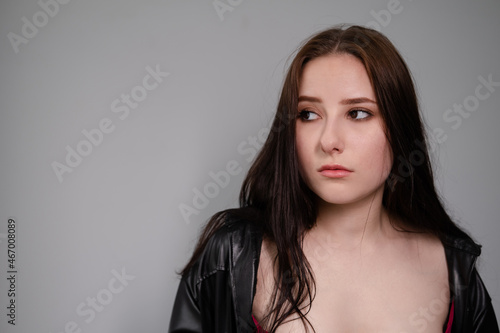 young brunette woman in black leather jacket. beautiful girl millenial on grey background.