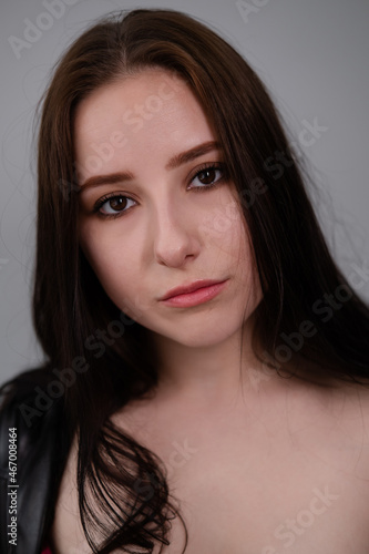 young brunette woman in black leather jacket. beautiful girl millenial on grey background.