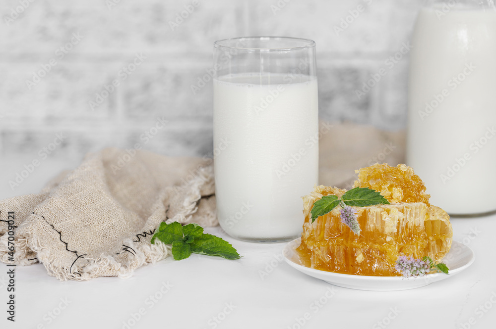 A still life of honey in honeycombs, a mint flower, a glass and a bottle of milk on a light background. A still life of honey in honeycombs, a mint flower, a glass and a bottle of milk on a light background.
