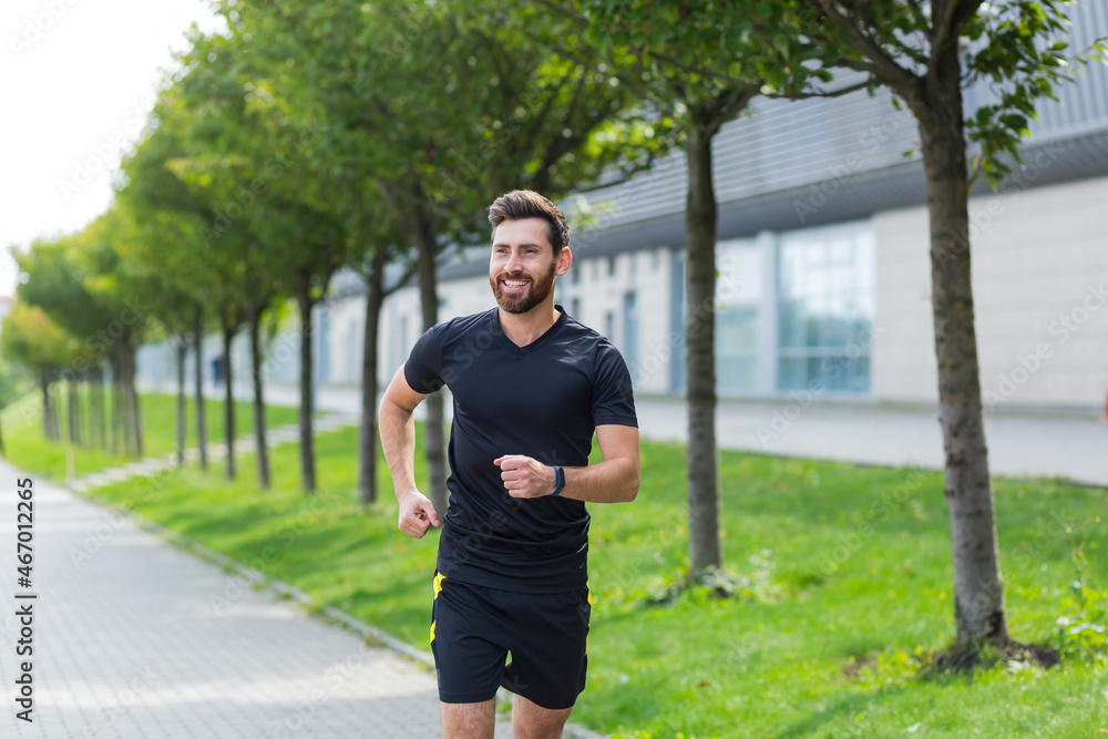 Young Caucasian bearded happy man runner jogging down the street on urban background of city park. Morning jog. Active healthy lifestyle fitness. Sport workout outdoor. Athlete training run exercise