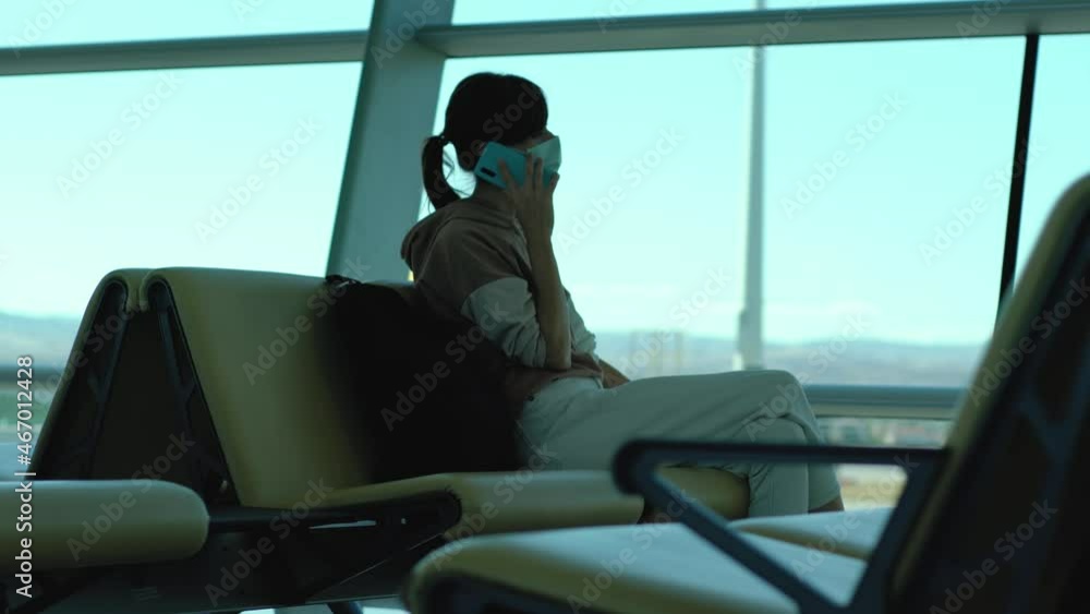Woman traveler in face mask talk by phone as waiting for departure in airport. Female traveler wait in departure terminal Woman traveler in face mask talk by phone as waiting for departure in airport. Female traveler wait in departure terminal