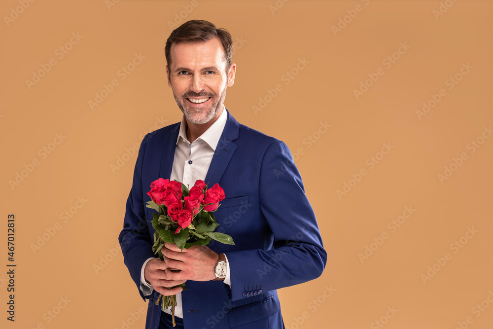 Handsome romantic business man in suit holding red roses in hand, smiling and looking to the camera. Handsome romantic business man in suit holding red roses in hand, smiling and looking to the camera.