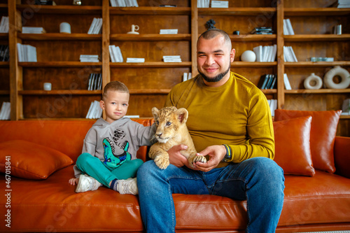 Father and son play with little lion cub in the room © popovatetiana