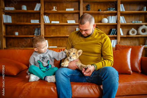 Father and son play with little lion cub in the room © popovatetiana