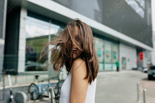 Happy european woman covering face by hair smiling broadly. Outdoor shot of wonderful well-dressed lady with dark hair.