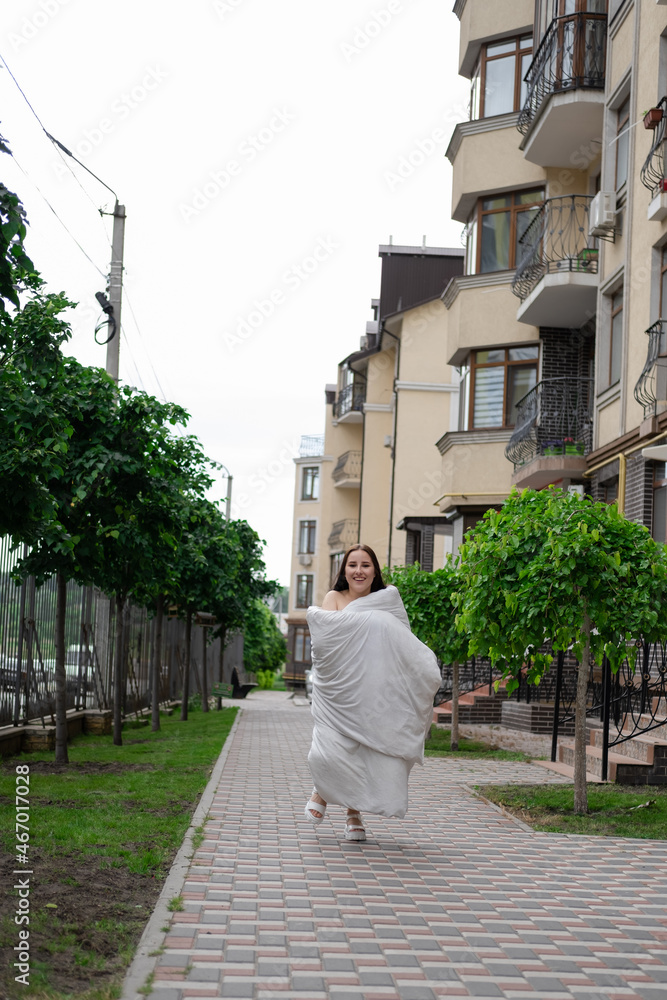 pretty brunette woman in white blanket on the street. crazy beautiful millennial carefree girl