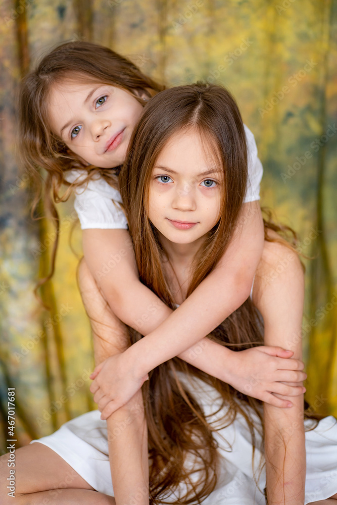 two little girls with long hair in white clothes cuddle. love between sisters. two little girls with long hair in white clothes cuddle. love between sisters.