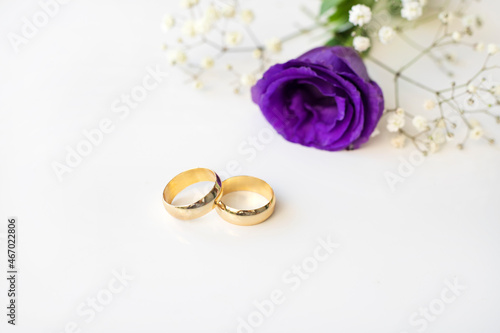 Purple flowers and two golden wedding rings on white background.