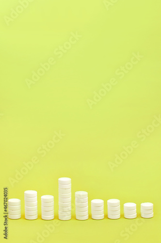 stacks of white pills on a yellow background in the form of a bar chart