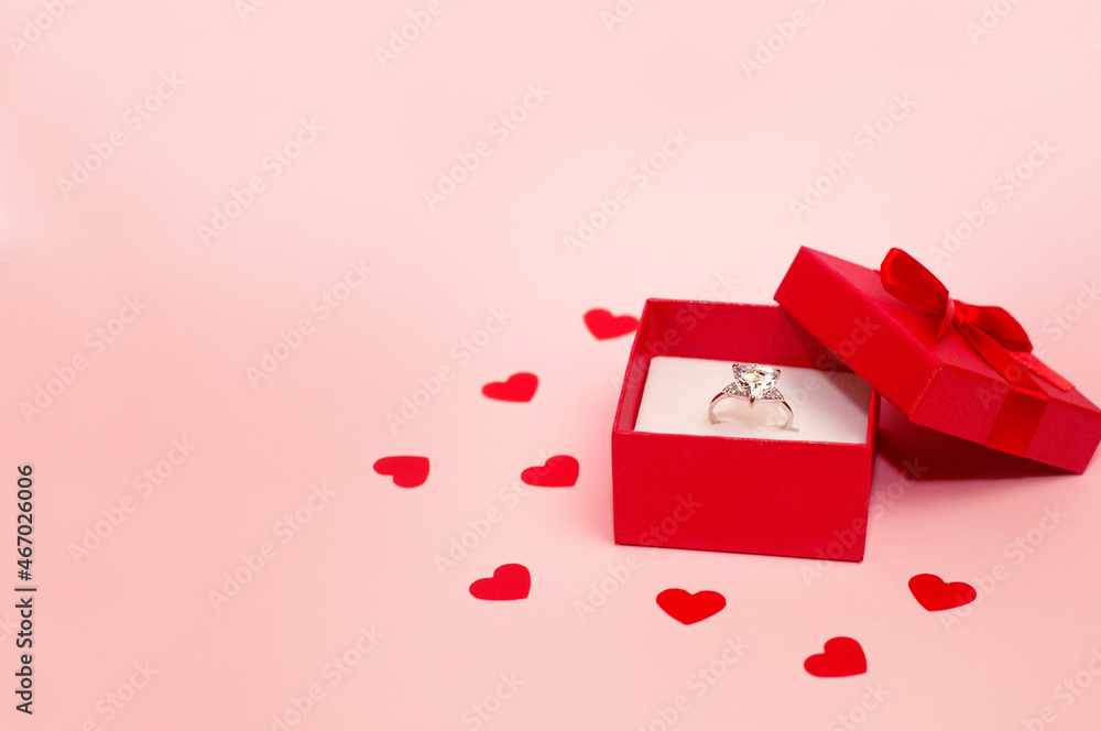 white gold ring with a large gemstone in a red box on a pink background with hearts
