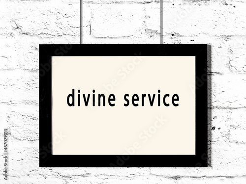 Black frame hanging on white brick wall with inscription divine service photo
