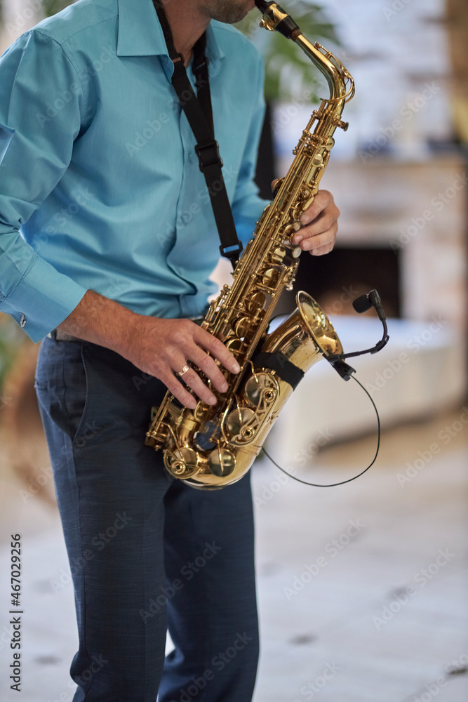 Naklejka premium A male saxophonist in a blue shirt plays the saxophone.