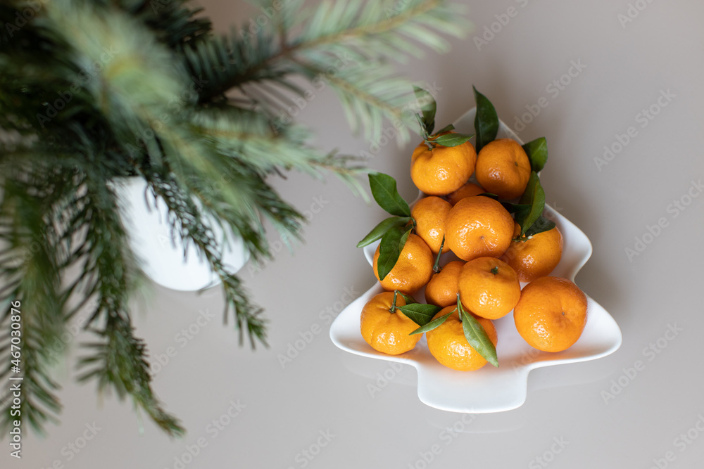 Small ripe tangerines with leaves, on plate in shape of Christmas tree on beige background. Concept winter vitamin food. Moody still life festive composition. For greeting card, book, stories Small ripe tangerines with leaves, on plate in shape of Christmas tree on beige background. Concept winter vitamin food. Moody still life festive composition. For greeting card, book, stories