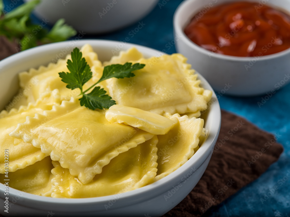 Delicious ravioli with a slice of butter and a parsley leaf. In the background are two sauces. Macro photography. Restaurant, cafe. Professional and home cooking.