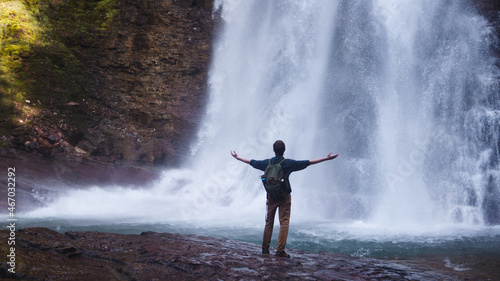 man standing at the base of a massive waterfall with arms outstretched