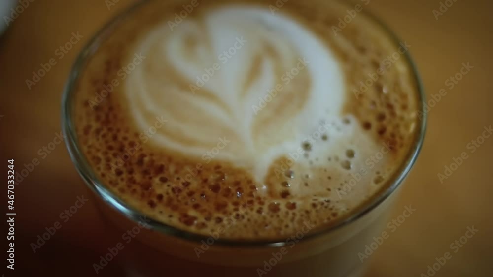 A man adds sugar cube in a cup of aromatic flat-white coffee. A cup of aromatic coffee is placed on a wooden table. A man adds sugar cube in a cup of aromatic flat-white coffee. A cup of aromatic coffee is placed on a wooden table.