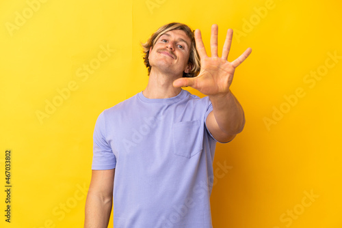 Handsome blonde man isolated on yellow background counting five with fingers