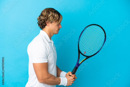 Young blonde man isolated on blue background playing tennis