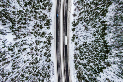 Aerial view of snow covered road in winter forest white truck driving by road seen from the air. Top view landscape. shooting from a drone. Cargo delivery in winter