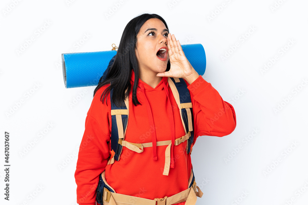 Young Colombian mountaineer girl with a big backpack isolated on white background shouting with mouth wide open Young Colombian mountaineer girl with a big backpack isolated on white background shouting with mouth wide open